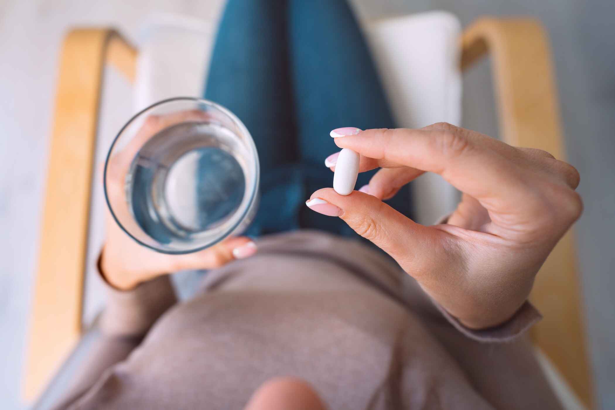 Eine Frau sitzt auf einem Stuhl. In der rechten Hand hält sie eine Tablette, in der linken Hand ein Glas Wasser.