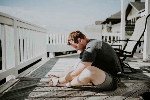 Bild eines Mannes auf einer Terrasse, der auf dem Boden sitzt und sich dehnt.
