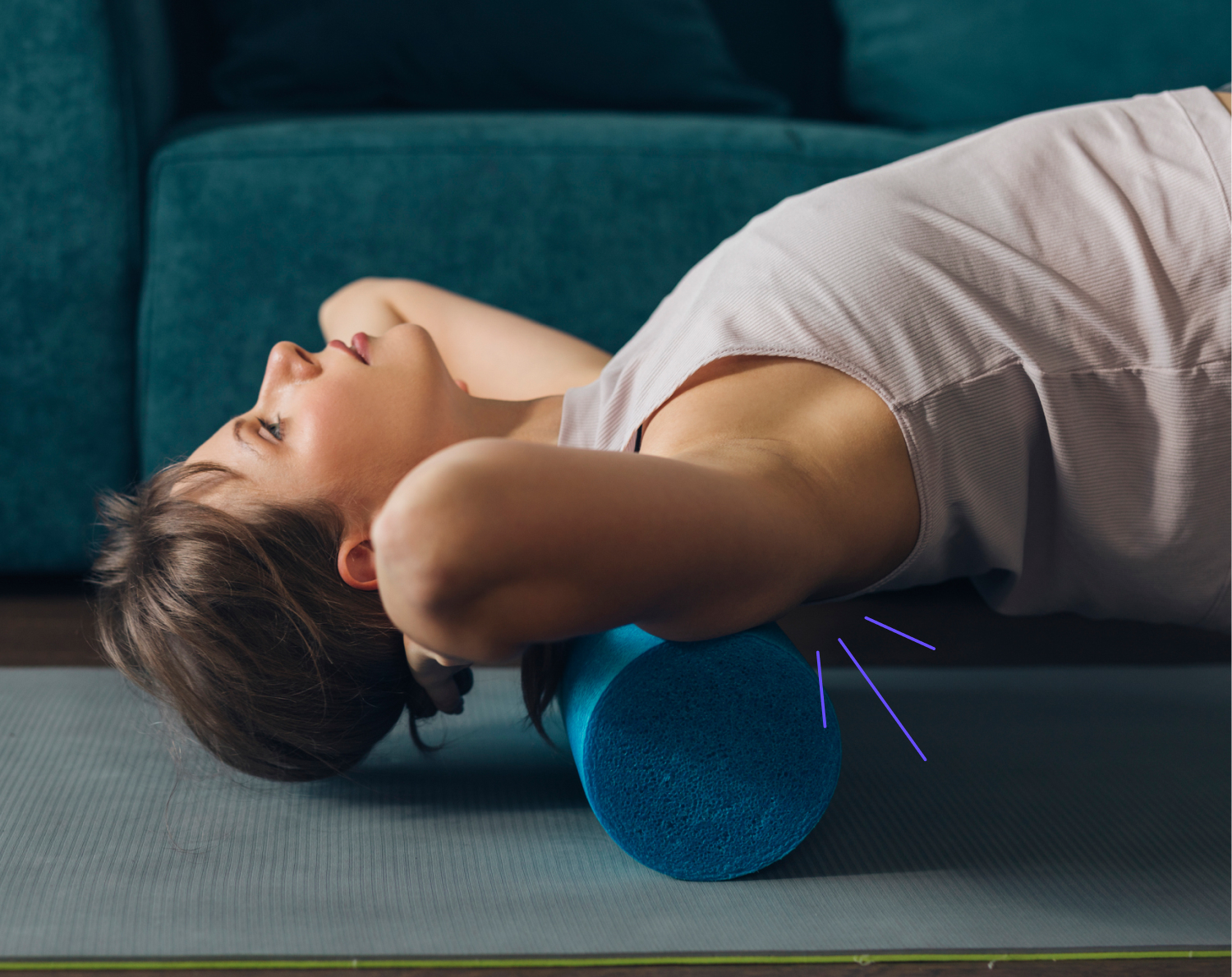 Eine Frau liegt auf einer Yogamatte und rollt ihren oberen Rücken auf einer blauen Faszienrolle aus. Sie löst damit Verklebungen der Faszien, um Rückenschmerzen zu lindern.