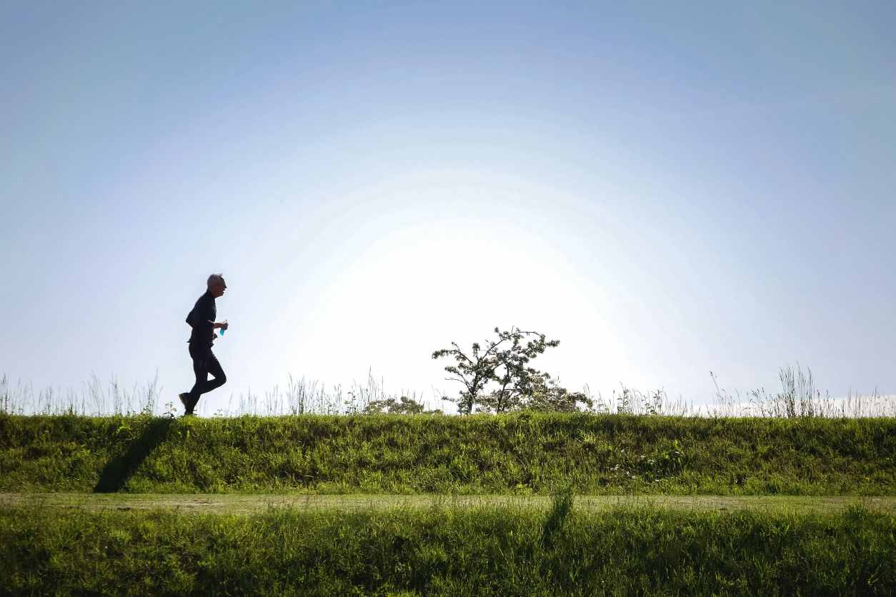 Bild von einem Mann der joggt. Der Himmel ist blau und der Boden von grünem Gras bedeckt.