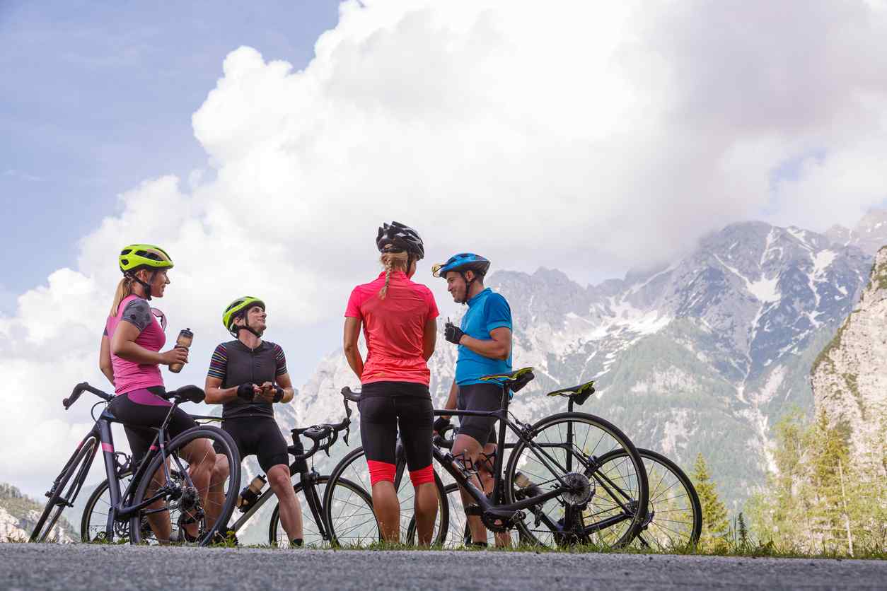 Eine Gruppe von Menschen mit Fahrradhelmen steht vor einer Bergkette mit ihren Rennrädern.